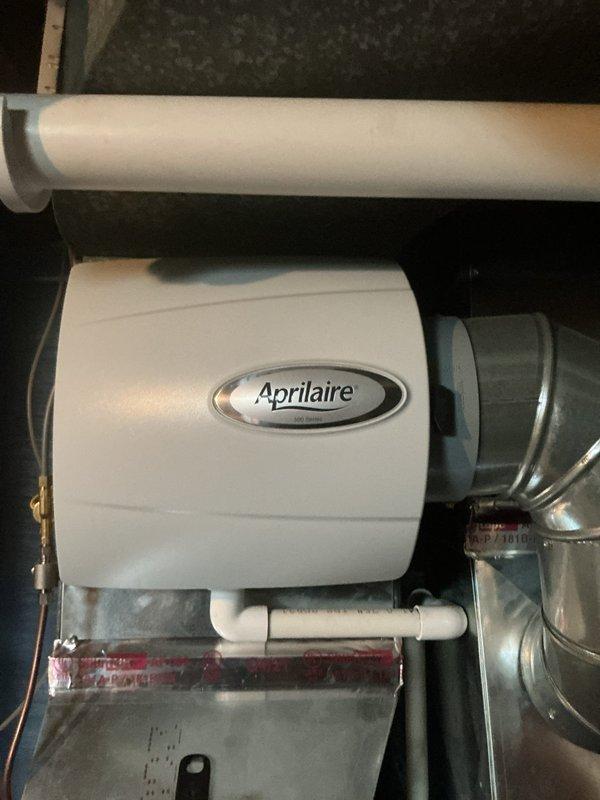 Completed comprehensive Gold AC inspection on 2-year-old outdoor condensing unit located in backyard against brick foundation. Performed full system evaluation including visual inspection of cabinet condition, fan operation, and electrical connections. Unit found in good operational condition with proper airflow through condenser coil and fan assembly functioning normally. Verified refrigerant lines secure and properly insulated, confirmed unit sitting level on protective base pad. Checked electrical disconnect box mounted on exterior wall for proper operation. Also inspected indoor Aprilaire humidifier system installed on ductwork in mechanical room, verified proper mounting and drainage configuration. All components operating within normal parameters with no immediate service needs identified. System ready for continued operation through cooling season.