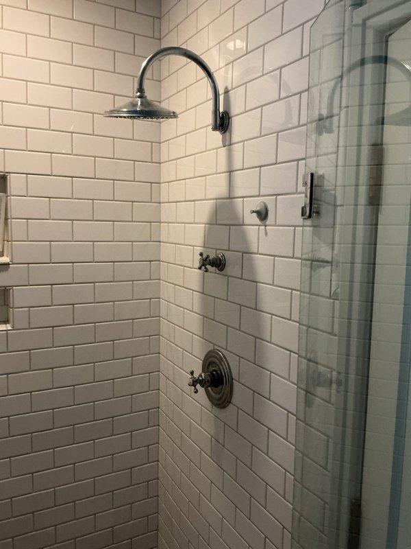 Responded to service call for dripping showerhead in residential bathroom. Upon inspection, identified leak originating from the rainfall-style showerhead mounted on gooseneck arm. Evaluated all shower fixtures including temperature control valve, diverter, and associated trim components to determine source of continuous drip. Tightened showerhead connection to gooseneck pipe and inspected internal washer for wear. Tested water flow and verified leak was eliminated. All fixtures returned to proper working condition with no active drips detected upon completion.