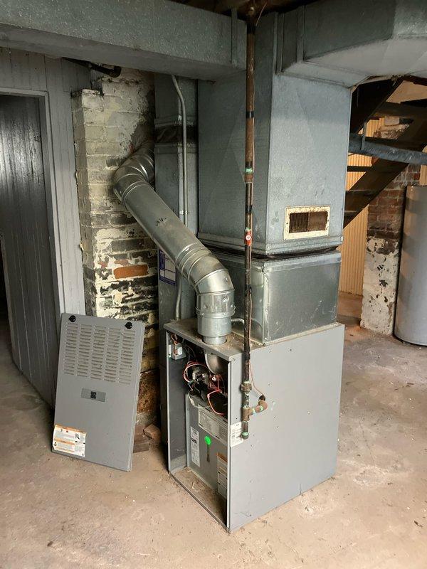 Responded to service call for non-operational hot water heater and furnace diagnostic evaluation in basement mechanical room. Performed comprehensive assessment of existing HVAC system including gray metal furnace unit with exposed internal components and white air handler assembly. Inspected ductwork connections, blower motor assembly, and ventilation system throughout basement area. Evaluated condition of copper piping, electrical connections, and overall system infrastructure. Documented equipment age and operational status through visual inspection with access panel removal. Assessed water heater functionality and provided recommendations for repair versus replacement options for both heating units based on current equipment condition and performance capabilities.