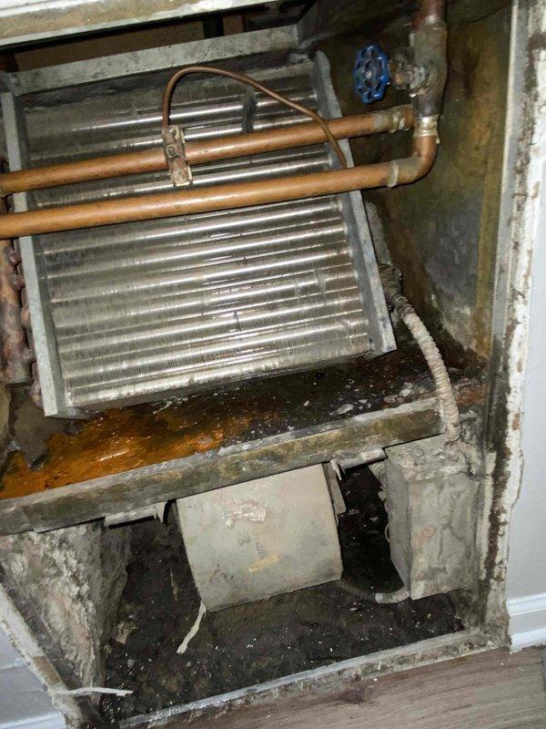 Responded to no heat call for 15-year-old boiler system in commercial unit. Upon inspection, identified leaking valve on copper piping assembly connected to heat exchanger coil, with significant corrosion and green patina indicating prolonged oxidation. Valve exhibited active leak with moisture accumulation in drain pan below unit. Documented existing conditions showing aged HVAC installation with deteriorated components and water damage to surrounding surfaces. Photographed corroded blue-handled valve, copper pipe connections, finned heat exchanger coil, and condensate management system for service records and repair recommendations.