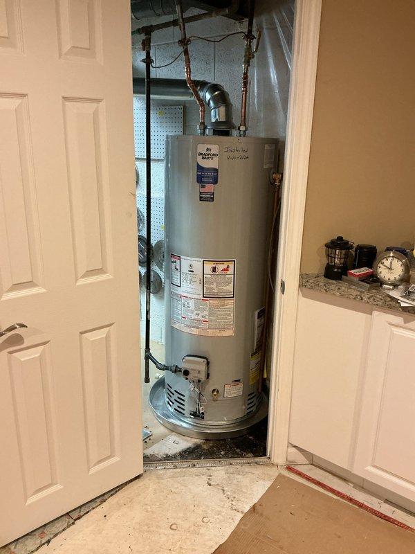 Installed 50-gallon standard capacity tanked water heater in residential utility closet with proper venting and plumbing connections. Unit was positioned on white plastic drain pan with alarm system for leak detection and safety compliance. Reconnected hot and cold water supply lines using copper piping, installed temperature and pressure relief valve assembly, and secured venting system with metallic elbow configuration for proper exhaust. All connections were tested for leaks and proper operation upon completion of installation.