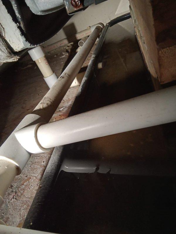 Responded to emergency call for water leaking from ceiling between second and third floors. Upon investigation, identified source of water intrusion in crawl space area beneath affected floors. Inspected white PVC drainage piping system running horizontally through the space, examining all elbow joints and connections for signs of failure or leakage. Assessed condition of plumbing infrastructure in utility area, including vertical drain lines and horizontal drainage configuration. Documented existing conditions showing accumulated moisture evidence on concrete surfaces and surrounding structural elements. Verified proper drainage flow and confirmed repair of compromised pipe section to eliminate active water leak. System tested and restored to normal operation, stopping water infiltration into ceiling cavity above.