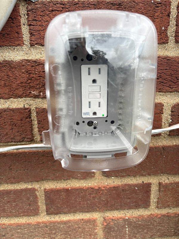 Installed weatherproof GFCI outlet on exterior brick wall to provide required electrical service within 25 feet of HVAC equipment, resolving city electrical code violation. Outlet features clear protective cover rated for outdoor use with proper sealing against moisture intrusion.