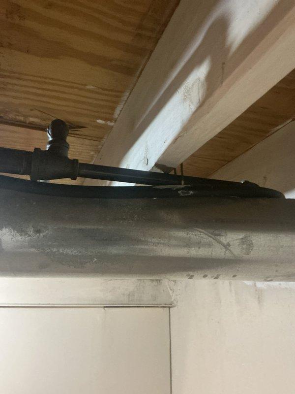 Completed gas line inspection and verification on water heater installation. Confirmed proper flexible gas connector installation with appropriate fittings and secure connections at both termination points. Verified gas valve assembly and burner compartment components are functioning correctly with no visible signs of leakage or deterioration. Inspected black iron gas piping run in basement area, confirming proper support and coupling integrity along horizontal run beneath floor joists. All gas connections tested and found to be secure with no safety concerns identified.