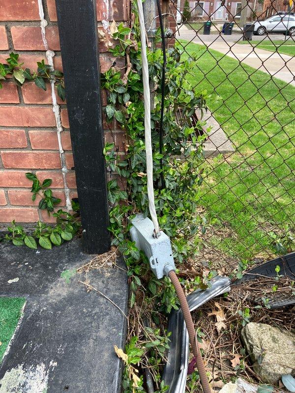 Conducted on-site evaluation for complete HVAC system replacement including outdoor air conditioning unit and basement furnace. Assessed existing cylindrical condenser unit located in narrow side yard between building and chain-link fence, documented equipment condition and installation specifications. Inspected electrical service routing along fence line, evaluated accessibility for replacement equipment, and photographed current system configuration to prepare comprehensive replacement estimate for both cooling and heating systems.