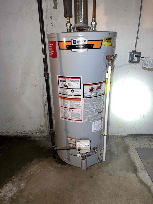 Responded to water leak call at residential property with water accumulation on top of water heater in basement. Performed diagnostic inspection of State ProLine water heater (10+ years old) and surrounding plumbing connections. Visual examination revealed corrosion and deteriorated material accumulation on mounting hardware and metal components, indicating long-term moisture exposure and potential leak source at pipe connections or fittings.