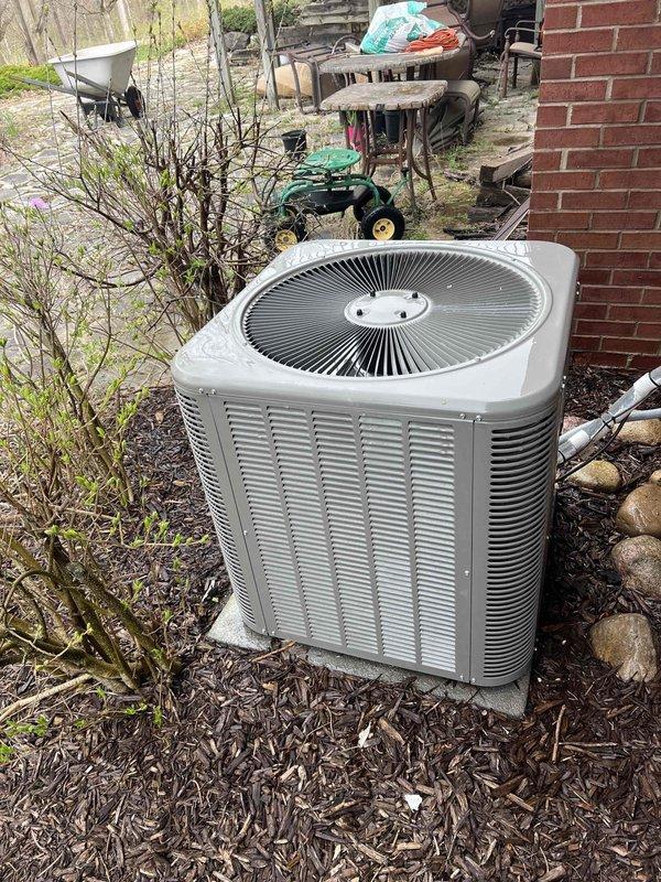 Completed comprehensive Gold AC inspection on 6-year-old residential cooling system with air handler located in basement. Performed thorough examination of outdoor condenser unit positioned on mulch bed adjacent to brick exterior, verified proper operation of fan assembly and protective grilles, inspected vertical louvered panels for adequate airflow, and assessed overall unit condition. Noted surrounding area contained debris including leaves, twigs, and branches that could potentially restrict airflow; documented equipment positioning and accessibility for future service requirements.