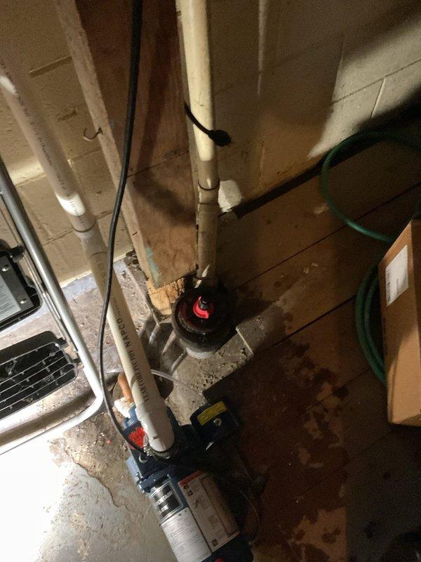 Responded to service call for basement water drainage concerns. Upon inspection, found existing sump pump system with visible floor staining indicating previous water infiltration issues. Evaluated PVC discharge piping configuration running from basement floor to exterior discharge point. Verified pump operation and assessed drainage patterns on concrete floor surface. Confirmed system functionality and provided recommendations for ongoing moisture management in below-grade space.
