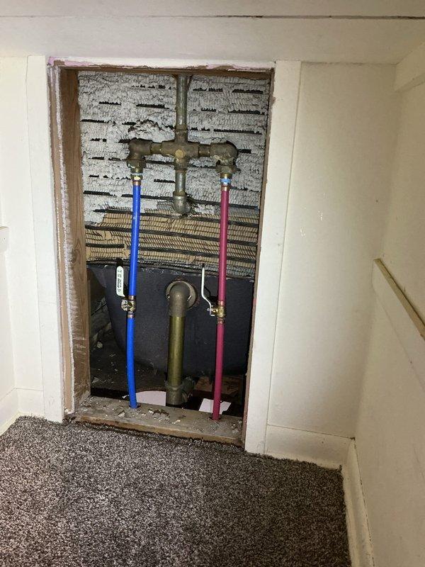 Responded to service call for shower valve conversion from three-valve to single-valve system. Performed diagnostic assessment of existing chrome-finished bathtub faucet assembly with three handles (two cross-handle valves and central diverter) mounted on white tile wall above vintage light blue bathtub. Accessed plumbing infrastructure through wall opening to inspect existing supply lines, including hot and cold water pipes with brass fittings and valves. Evaluated current configuration and measured installation parameters. Provided detailed quote for converting three-valve system to modern single-valve shower control unit, including necessary modifications to existing plumbing connections and wall preparation requirements.