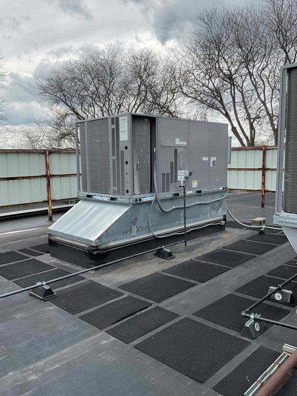 Accessed commercial rooftop to document existing HVAC equipment installation for inspection purposes. Photographed two rooftop package units mounted on metal curb adapters with proper EPDM roofing membrane and walkway pad configuration, capturing equipment condition, refrigerant line routing, electrical disconnects, and surrounding rooftop infrastructure as requested.