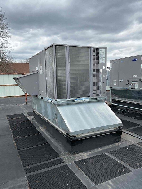 Accessed commercial rooftop to document existing HVAC equipment installation for inspection purposes. Photographed two rooftop package units mounted on metal curb adapters with proper EPDM roofing membrane and walkway pad configuration, capturing equipment condition, refrigerant line routing, electrical disconnects, and surrounding rooftop infrastructure as requested.
