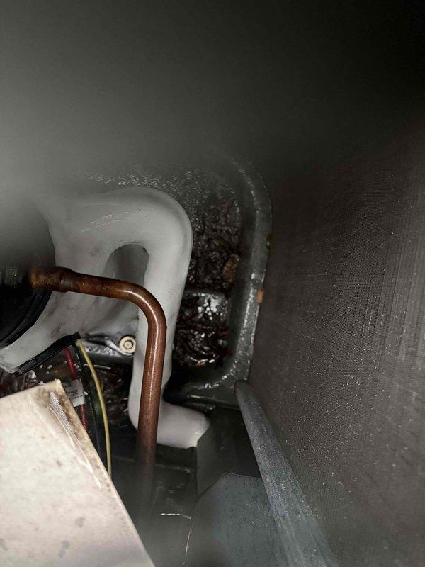 Responded to service call for central air conditioning system running but producing little to no airflow through vents with no cooling capacity. Upon inspection, discovered severely clogged evaporator drain pan with excessive accumulation of dirt, biological growth, and sediment blocking proper drainage and restricting airflow. Cleaned and cleared drain pan assembly, removed debris buildup from drain opening, and restored proper condensate drainage function. Verified system operation with adequate airflow restored through all vents and cooling capacity returned to normal parameters.