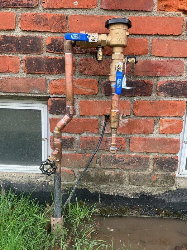 Completed annual testing and certification of PVB (Pressure Vacuum Breaker) backflow preventer assembly mounted on exterior brick wall. Inspected backflow device with identification tag T694119, verified proper operation of vacuum breaker mechanism and brass valve assembly, confirmed all components functioning within specifications. Documented installation with photographs showing complete assembly including Zurn ball valves, copper piping configuration, and proper mounting to building exterior for compliance records.