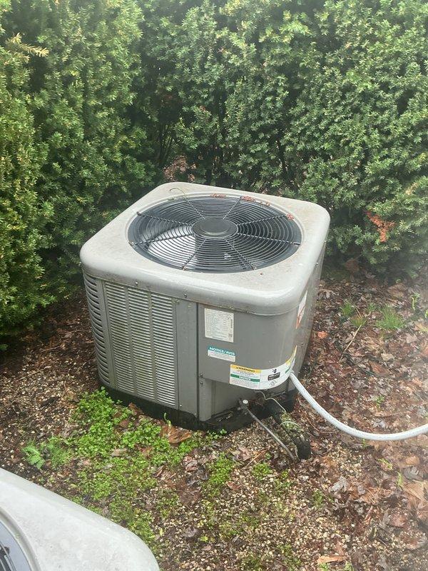 Responded to no cooling complaint on residential property with multiple HVAC systems. Upon arrival, located and inspected three outdoor condenser units positioned on gravel pad with adequate clearance. Units showed signs of normal wear with debris accumulation on top surfaces including leaves and dirt. Verified all condensers were beige-colored cabinet style units with wire fan guards and louvered side panels for proper ventilation. Noted condensate drainage lines present and vegetation growth in close proximity to equipment. Documented equipment condition through photography showing manufacturer labels and warning stickers visible on unit panels. All units appeared to be standard residential split-system configurations with top-discharge fan assemblies mounted on concrete pads with gravel surround for drainage.