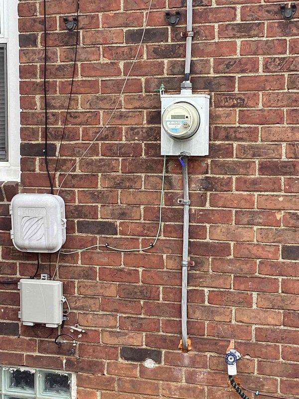 Conducted comprehensive site assessment for HVAC system replacement at residential property. Documented existing exterior electrical infrastructure including meter box, junction panels, and conduit routing on brick exterior wall to ensure proper coordination with new HVAC equipment installation. Evaluated interior basement area conditions, noting unfinished walls with moisture concerns and existing utility routing that will require consideration during equipment placement and ductwork installation.