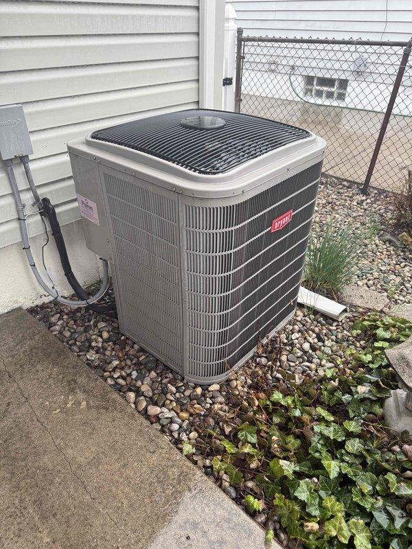 Completed comprehensive Gold AC inspection on 24-year-old Bryant air conditioning system with air handler located in basement. Performed visual inspection of outdoor condenser unit, confirming proper placement on concrete pad with adequate clearance and drainage provided by surrounding gravel bed. Verified unit operational status, inspected exterior cabinet condition showing no visible damage, rust, or deterioration to fins and housing. Checked electrical connections and conduit routing to disconnect box. Confirmed condenser coil fins in good condition with proper airflow access. Inspected top grille and fan assembly housing for structural integrity. Verified landscaping debris clearance around unit perimeter to maintain proper airflow and prevent obstruction. System found operational with homeowner confirming cooling functionality prior to inspection.