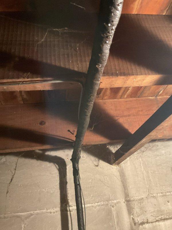 Responded to leaking main waterline in basement of century-old residential property. Upon inspection, identified active leak at vertical pipe penetration point where main water supply line emerges from basement floor. The compromised section exhibited deteriorated insulation wrapping and visible water seepage around pipe-to-floor junction. Shut off water supply at main gate valve near meter assembly to stop active leak. Assessed copper piping system and water meter installation mounted on concrete block foundation wall. Documented existing conditions including aged plumbing infrastructure, corroded pipe coverings, and water damage to surrounding concrete floor area. Recommended complete replacement of affected main line section due to age-related deterioration and potential for future failure in adjacent piping.