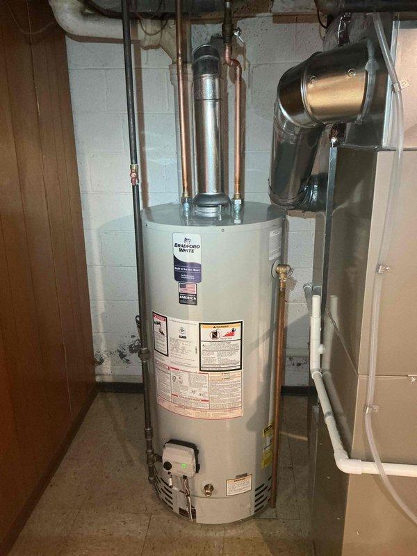 Completed installation of Bradford White residential tanked water heater in basement utility area. Unit was properly positioned on drain pan, connected to existing copper supply lines and exhaust venting system with appropriate fittings and hardware. Mechanical permit was requested and all plumbing connections, safety valves, and ventilation components were installed per code requirements to restore hot water service to the residence.