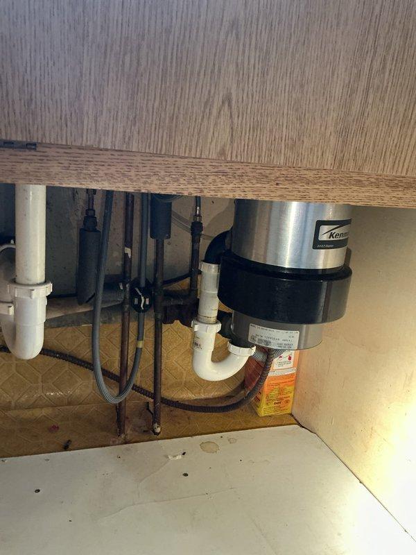 Installed new Kenmore garbage disposal unit under kitchen sink in 67-year-old residential home. Removed existing disposal, mounted new unit to sink drain flange, connected white PVC P-trap drainage system, and completed electrical wiring connections. Tested unit for proper operation and verified all plumbing connections were secure with no leaks.