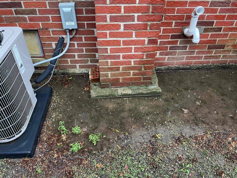 Completed comprehensive Gold AC inspection on 9-year-old residential HVAC system with furnace located in basement. Performed thorough evaluation of outdoor condensing unit positioned on concrete pad against exterior brick wall, confirming operational status of fan motor assembly, capacitor, and electrical connections. Inspected condenser coil protection mesh, verified proper airflow through intake panels, and assessed electrical conduit routing to junction box mounted on building exterior. Documented unit condition with photographic evidence showing functional components, weathered concrete pad with minor debris accumulation, and PVC drainage line installation. Confirmed single-unit residential system is operating as designed with homeowner present during inspection.