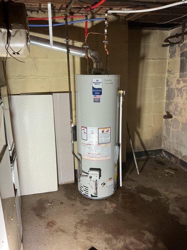 Completed installation of a 40-gallon residential gas-fired water heater in basement utility area. Unit was positioned on concrete floor against cinder block wall with all plumbing connections made using copper piping at inlet and outlet points, brass fittings and valves installed at top connections, and gas line reconnected per code requirements. All manufacturer labels and safety information remain visible and intact on exterior of unit.