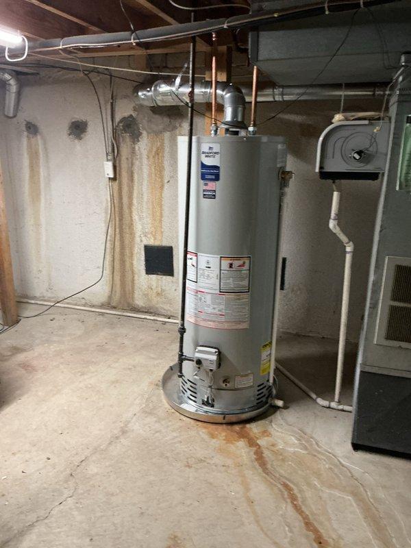 Responded to water leak complaint near recently installed water heater. Upon inspection, identified active water intrusion evidenced by rust-colored staining and water trails on concrete basement floor extending from water heater base. Examined PVC drainage piping in overhead floor cavity and water heater connections, including copper supply lines and metallic vent pipe. Documented condition of plumbing assembly, connections, and surrounding areas with photographic evidence. Water heater installation and associated plumbing connections were assessed for proper installation and potential leak sources.