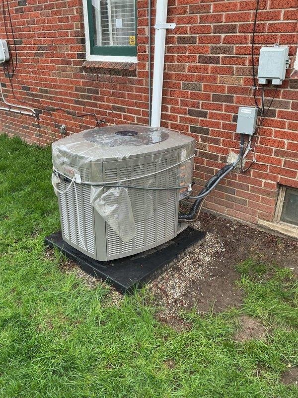 Responded to concerns regarding a 6-month-old AC condenser unit that had shifted position following recent rainfall. Upon inspection, found the unit had experienced minor displacement on its pad due to water infiltration beneath the platform base. Verified the condenser was still level and operational with no damage to refrigerant lines, electrical connections, or structural components. Documented the unit's current positioning and condition with photographs showing the installation against the brick exterior, including the electrical disconnect, conduit routing, and pad placement on the gravel base. Confirmed all mounting hardware remained secure and unit was functioning properly despite the slight movement. Recommended monitoring the pad stability and considering enhanced drainage or pad reinforcement to prevent future displacement during heavy rain events.
