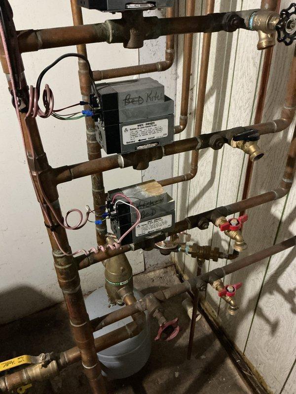 Responded to service call regarding damaged thermostat wiring in heating system. Upon inspection, located cut thermostat wire connected to zone control modules in multi-zone hydronic heating system. Assessed the control panel configuration with multiple zone valves and verified extent of wire damage. Documented existing conditions of copper piping network, zone control boxes with visible blue and red wiring connections, and overall system layout for repair planning and future reference.