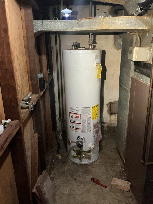 Responded to service call for water heater replacement estimate and pipe repair following damage caused by unpermitted installation attempt. Assessed existing natural draft gas water heater unit in basement utility alcove and identified broken piping requiring replacement. Evaluated installation area including concrete block enclosure, overhead plumbing infrastructure, and existing gas and water supply connections. Provided estimate for complete removal of damaged unit and installation of new 40-60 gallon natural draft gas water heater with proper pipe repairs and code-compliant connections to restore hot water service.