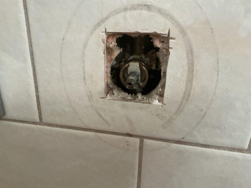 Responded to service call for no hot water pressure at shower fixture. Upon investigation, accessed plumbing behind shower valve through existing wall opening and discovered obstruction affecting hot water supply line. Inspected shower valve assembly and associated plumbing connections, identifying issue with hot water delivery to the shower head and handheld spray unit. Documented existing conditions showing signs of previous water damage and corrosion around valve access point.