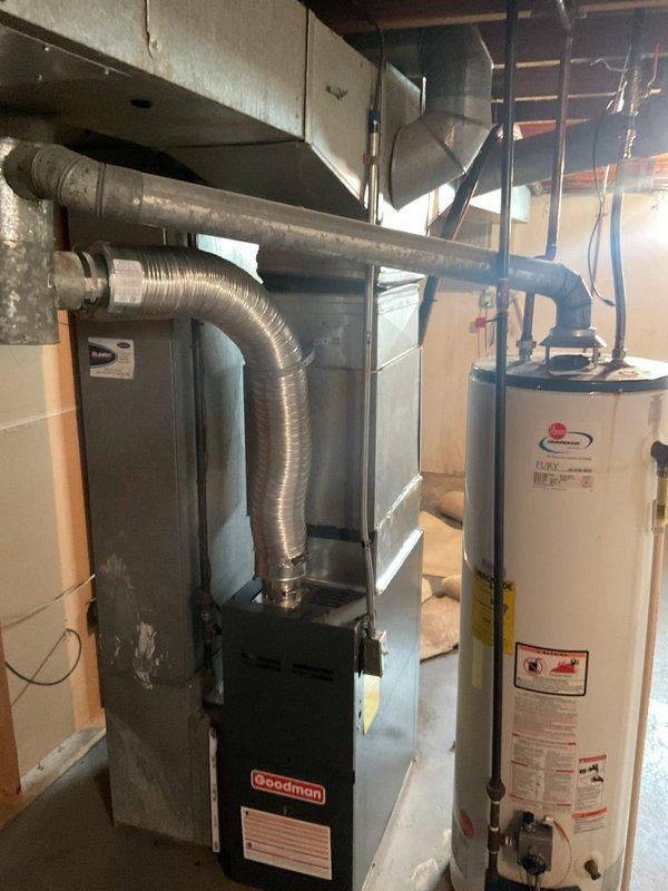 Responded to service call for reported corroded exhaust pipe with visible hole. Upon arrival, conducted thorough inspection of basement utility area housing Goodman furnace unit and tanked water heater. Examined metal ductwork system, exhaust venting components, and flue pipe connections for signs of corrosion, deterioration, or breach points. Assessed condition of HVAC exhaust infrastructure, noting surface discoloration and age-related wear on metal ductwork and ventilation components. Documented equipment configuration and current state of exhaust system through photographic documentation. Evaluated structural integrity of venting system, mounting hardware, and connection points to identify source of reported corrosion issue and determine appropriate repair or replacement recommendations.