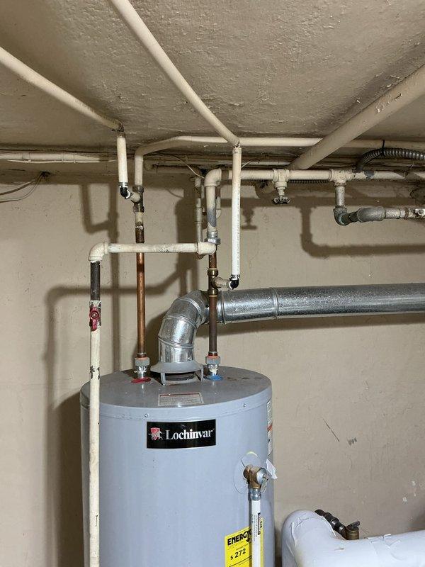 Conducted on-site assessment of existing plumbing system in 1930s-era residential property to provide estimate for galvanized pipe replacement. Inspected basement utility area and documented current plumbing infrastructure, including water heater connections, supply lines, and distribution piping throughout the space. Observed mixed piping materials consisting of older galvanized steel pipes, copper supply lines, and newer PVC drainage systems. Photographed existing Lochinvar water heater installation with associated hot and cold water connections, noting current configuration of metallic and PVC piping runs along ceiling joists. Evaluated condition of visible galvanized piping to determine scope of replacement work needed to bring plumbing system up to current standards and prevent future corrosion-related failures common in homes of this vintage.