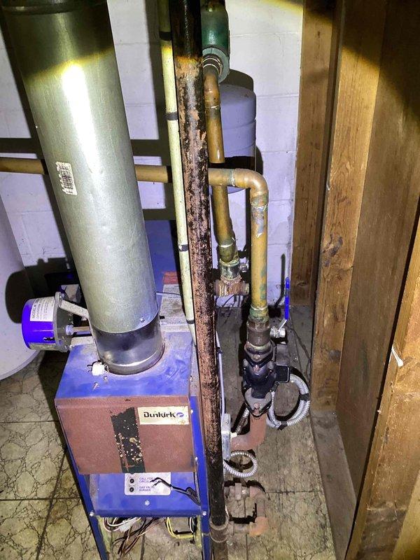Responded to service call for non-functioning hot water boiler in basement. Upon inspection, determined 21-year-old Dunkirk boiler was unsafe to operate due to improper ignition and extensive corrosion throughout the system, particularly on vertical piping and connections. Unit displayed three indicator lights but failed to light properly. Documented existing conditions showing significant rust deterioration on piping components and aging infrastructure. Provided comprehensive estimate for boiler replacement due to safety concerns and equipment age exceeding serviceable lifespan.