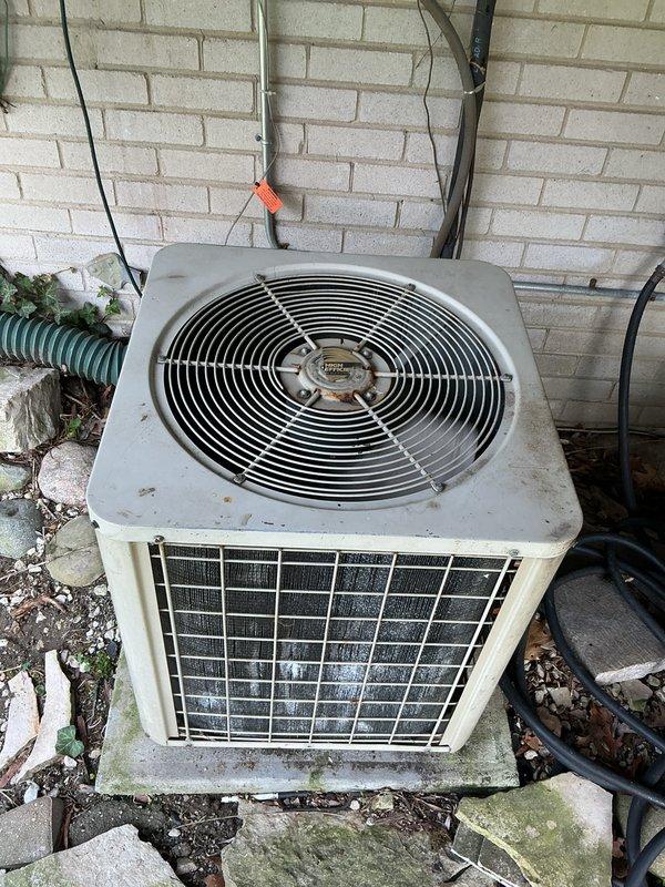 Completed comprehensive Gold AC inspection and maintenance on outdoor condensing unit showing signs of age and weathering. Performed standard tune-up procedures including inspection of condenser coils, fan assembly, and refrigerant lines. Successfully installed customer-provided thermostat in living room to replace existing unit. Condenser unit exhibited dirt accumulation on exterior surfaces and protective grilles, with minor surface deterioration and algae growth on concrete pad. All electrical connections, refrigerant lines, and mounting hardware inspected and found secure. Fan guard and blade assembly operational. System tested and confirmed functioning properly following maintenance and thermostat installation.