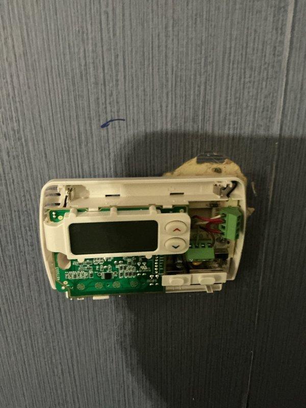 Responded to service call for Honeywell digital thermostat not responding to temperature setting adjustments on 2-week-old equipment located on main floor. Performed diagnostic inspection, removed thermostat cover to examine internal circuit board, wiring connections, and LCD display components. Verified proper power supply connections via red and black wiring, inspected green circuit board for defects, and tested thermostat functionality to identify and resolve temperature control issue.