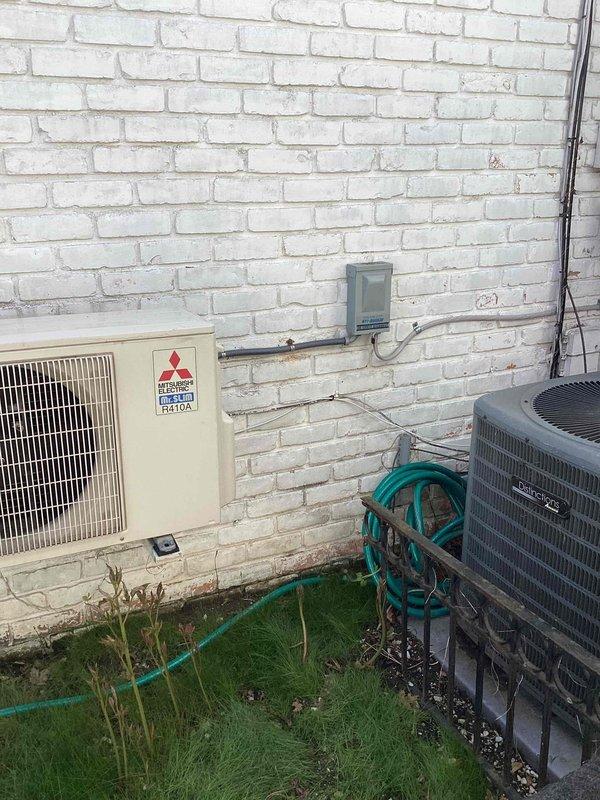 Provided estimate for replacement of two aging HVAC units: a 20+ year old Mitsubishi mini-split heat pump (model FH410A) showing signs of mold growth, and a 30-year-old air conditioning system with low R22 refrigerant levels. Both outdoor units are located in the backyard area along the exterior brick wall. The mini-split system requires replacement due to mold contamination, while the traditional AC condenser unit is experiencing refrigerant loss in an obsolete R22 system. Documented existing installation configuration including electrical connections, conduit routing, and equipment placement on concrete pads for replacement planning purposes.