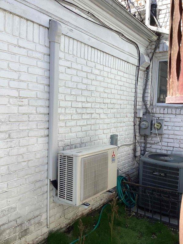 Provided estimate for replacement of two aging HVAC units: a 20+ year old Mitsubishi mini-split heat pump (model FH410A) showing signs of mold growth, and a 30-year-old air conditioning system with low R22 refrigerant levels. Both outdoor units are located in the backyard area along the exterior brick wall. The mini-split system requires replacement due to mold contamination, while the traditional AC condenser unit is experiencing refrigerant loss in an obsolete R22 system. Documented existing installation configuration including electrical connections, conduit routing, and equipment placement on concrete pads for replacement planning purposes.