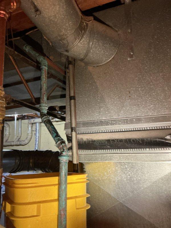 Responded to active water leak in basement originating from area above Bradford White water heater. Upon inspection, identified moisture and condensation on metallic exhaust flue pipe extending from top of water heater unit. Leak had been present for several weeks with recent worsening, contained to immediate vicinity by floor drain. Examined all plumbing connections including copper supply lines with brass fittings and dielectric union, PVC discharge piping, and surrounding utility infrastructure including yellow condensate pump and associated drainage systems. Assessed water heater installation in 1973-era home with concrete block foundation. Documented conditions with photographic evidence showing wet flue pipe, plumbing configuration, and mechanical systems layout. Confined water damage to immediate area around water heater with proper drainage preventing spread throughout basement.