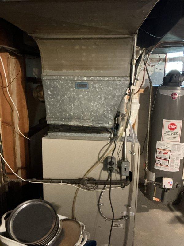 Conducted on-site assessment of existing HVAC system in residential basement mechanical room to provide replacement estimate. Evaluated current furnace unit with white cabinet base and galvanized metal plenum, noting configuration of existing ductwork connections including flexible black duct at upper plenum. Documented electrical service routing and conduit placement for equipment replacement planning. Assessed available clearances around existing equipment, including proximity to water heater and surrounding plumbing infrastructure. Examined overhead ductwork, copper piping, and PVC drain lines to determine any modifications needed for new equipment installation. Photographed current system layout and mechanical room conditions to support accurate equipment sizing and replacement proposal for both furnace and air conditioning components.