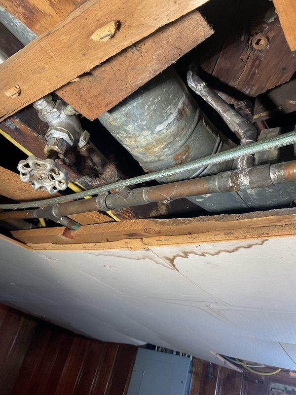 Responded to a plumbing service call to address aging galvanized water supply lines and under-sink drainage concerns. Inspected attic/crawl space plumbing infrastructure where corroded galvanized pipes, deteriorated shut-off valves, and oxidized fittings were identified as potential failure points requiring monitoring or replacement. Examined under-sink cabinet area where PVC drain assembly and P-trap were assessed for proper function, noting previous water staining on cabinet floor indicating past leak history. Documented existing plumbing conditions with photographic evidence for service records and provided recommendations for future maintenance to prevent water damage.