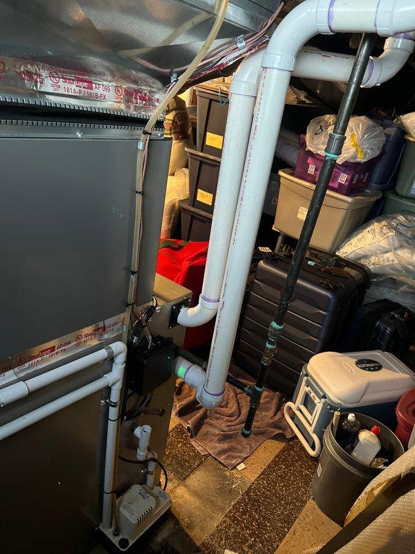 Completed installation of a 2-ton air conditioning system with matching evaporator coil. The outdoor condensing unit was positioned on a rubber isolation pad on the left side of the property against the brick exterior wall, with proper electrical disconnect box mounted above and refrigerant lines and conduit secured to the wall. The indoor air handler was installed in the basement utility area with appropriate drainage piping and electrical connections. All mechanical, electrical, and air conditioning permits were requested and the system was reconnected and tested for proper operation.