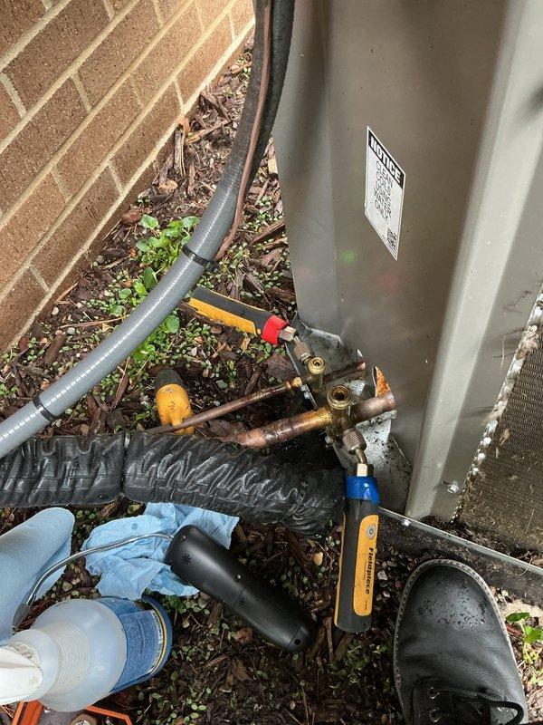 Returned to property to perform comprehensive leak search on 2-year-old outdoor air conditioning unit experiencing no cooling condition. Utilized electronic leak detector and nitrogen pressure testing with flame torch to identify refrigerant leak points in system. Inspected condenser unit, refrigerant line connections, and compressor assembly for potential leak sources. Noted significant debris accumulation in drain pan and surrounding outdoor unit area that could impact system performance. Documented equipment condition and leak search findings with photographs for service records.