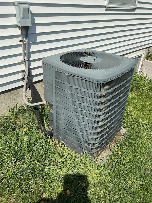 Completed comprehensive Gold AC inspection on single residential air conditioning system with equipment under 10 years old and air handler located in basement. Performed thorough examination of outdoor condenser unit, which showed normal operational wear with dust and dirt accumulation on metal fins and housing. Verified unit functionality and proper operation of all components including condenser coils, fan assembly, and electrical connections. Inspected refrigerant lines, electrical disconnect box, and PVC conduit for proper installation and condition. Confirmed condenser unit remains level on concrete pad with adequate clearance, though noted some grass growth and minor debris accumulation around base of unit and pad perimeter. System operating within normal parameters at time of inspection.