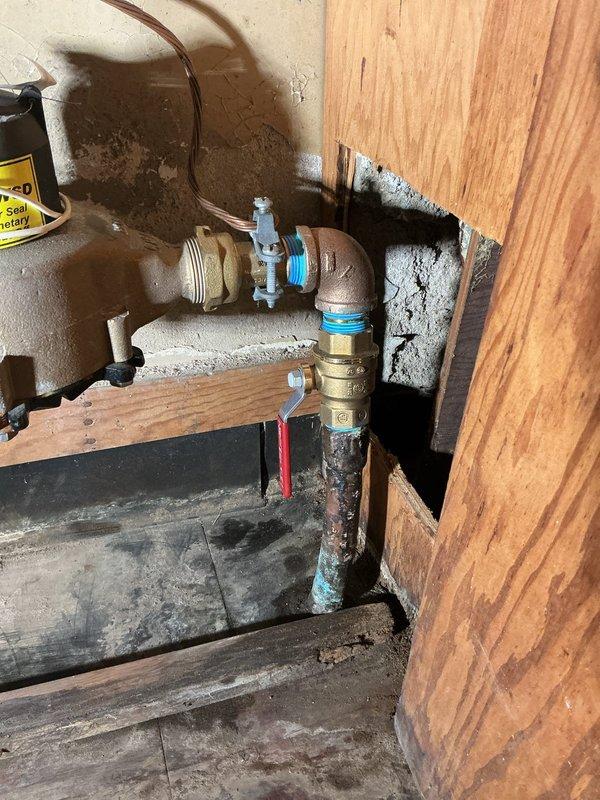 Responded to emergency service call for city water shutoff at residential property. Upon arrival, inspected basement plumbing system and documented existing conditions showing aged copper and brass piping with multiple fittings, valves, and significant corrosion at connection points. The vertical brass pipe assembly displayed blue-green copper oxidation and mineral deposits indicating prolonged water exposure. Observed moisture staining on surrounding surfaces and extensive efflorescence buildup at foundation penetrations. Tagged affected plumbing components with warning labels and photographed deteriorated areas for documentation purposes. Coordinated with property contact regarding water shutoff status and provided assessment of plumbing conditions requiring attention.