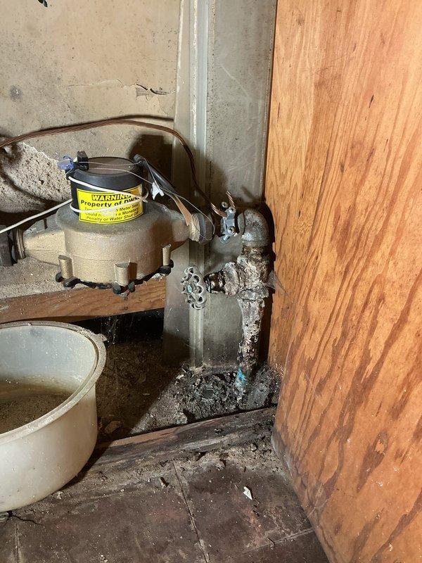 Responded to emergency service call for city water shutoff at residential property. Upon arrival, inspected basement plumbing system and documented existing conditions showing aged copper and brass piping with multiple fittings, valves, and significant corrosion at connection points. The vertical brass pipe assembly displayed blue-green copper oxidation and mineral deposits indicating prolonged water exposure. Observed moisture staining on surrounding surfaces and extensive efflorescence buildup at foundation penetrations. Tagged affected plumbing components with warning labels and photographed deteriorated areas for documentation purposes. Coordinated with property contact regarding water shutoff status and provided assessment of plumbing conditions requiring attention.