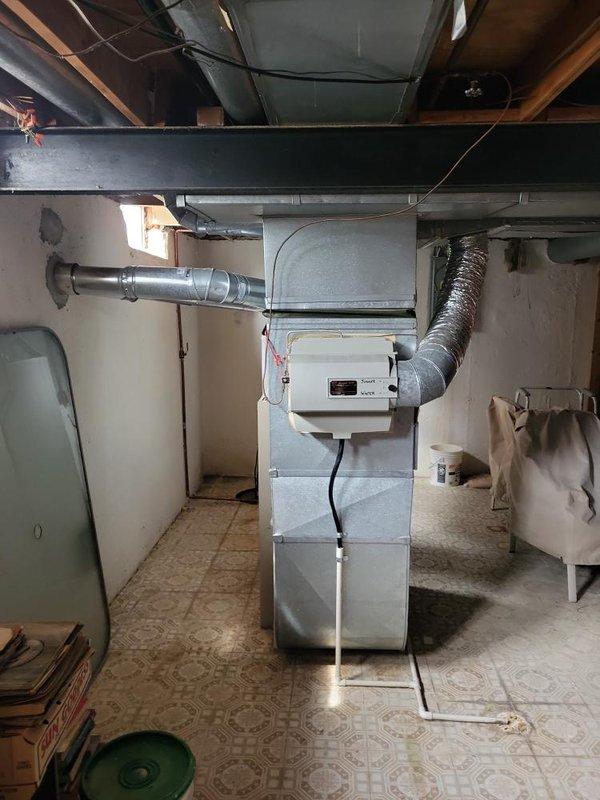 Completed comprehensive HVAC system evaluation for replacement estimate on aging residential equipment including 1980s-era air conditioning unit low on R22 refrigerant and 1997 furnace with documented venting issues causing flame rollout concerns. Documented exterior condenser unit positioned on concrete pad with associated refrigerant lines and electrical connections, and basement furnace installation with ductwork configuration to provide accurate replacement specifications for complete system upgrade.
