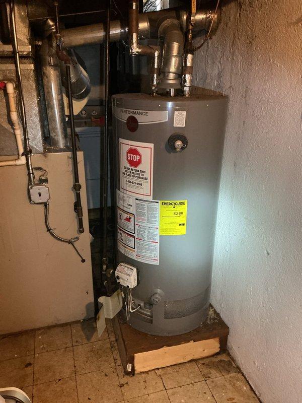 Responded to water heater leak reported at bottom of unit. Upon inspection, confirmed active leakage from base of residential water heater tank, indicating internal tank failure. Documented existing installation elevated on wooden platform with copper supply lines and proper venting connections. Assessed surrounding floor area showing water damage and drainage conditions. Provided estimate for complete water heater replacement including removal of failed unit, installation of new tank with code-compliant connections, and proper disposal of old equipment.