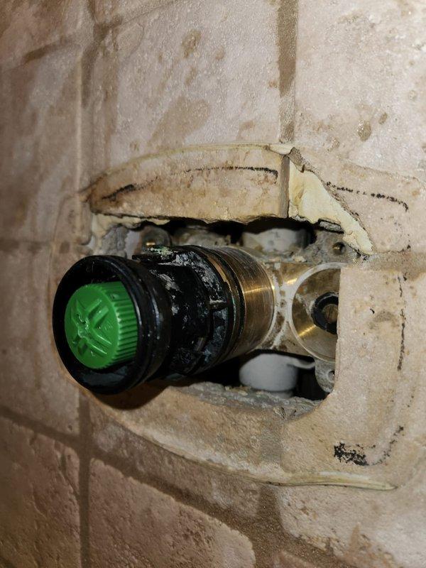 Responded to service call for no hot water to shower, toilet issue, and basement leak. Upon inspection, identified failed shower valve cartridge with significant wear, discoloration, and mineral buildup on the valve stem assembly. The cartridge showed brownish residue and deterioration at the base, preventing proper hot water flow control. Additionally, discovered damaged tile work surrounding the shower valve with broken sections exposing substrate, water staining, and mineral deposits indicating previous leak activity. Removed worn cartridge assembly from brushed metal escutcheon plate and replaced with new valve cartridge to restore hot water function. Addressed underlying plumbing concerns contributing to basement leak by repairing compromised valve connections. Recommend future tile repair around fixture to prevent moisture intrusion and further wall damage.