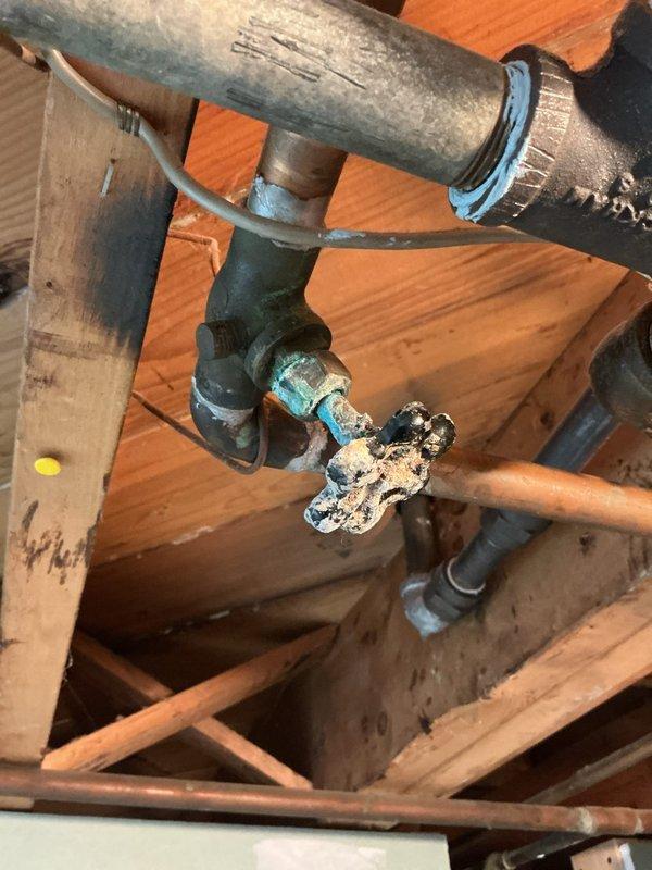 Conducted thorough inspection of existing basement plumbing system to provide comprehensive piping estimate. Assessed multiple corroded components including heavily oxidized gate valve with deteriorated blue handle showing advanced turquoise and white corrosion patterns, indicating prolonged moisture exposure. Evaluated aging galvanized steel and copper pipe configuration throughout exposed wooden joist structure, documenting significant green-blue oxidation on copper fittings, weathered pipe connections, and compromised valve assembly requiring replacement to ensure system integrity and prevent potential water supply failures.