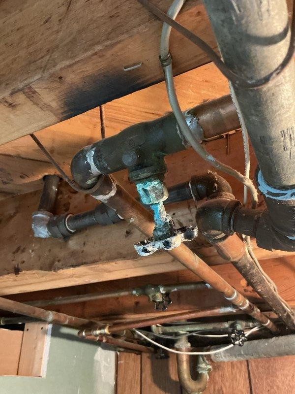 Conducted thorough inspection of existing basement plumbing system to provide comprehensive piping estimate. Assessed multiple corroded components including heavily oxidized gate valve with deteriorated blue handle showing advanced turquoise and white corrosion patterns, indicating prolonged moisture exposure. Evaluated aging galvanized steel and copper pipe configuration throughout exposed wooden joist structure, documenting significant green-blue oxidation on copper fittings, weathered pipe connections, and compromised valve assembly requiring replacement to ensure system integrity and prevent potential water supply failures.